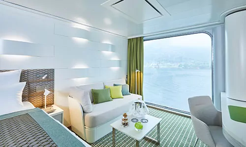 Schlaf- und Wohnbereich mit Blick aus dem Panoramafenster auf dem Luxusexpeditionsschiff HANSEATIC nature der Reederei Hapag-Lloyd