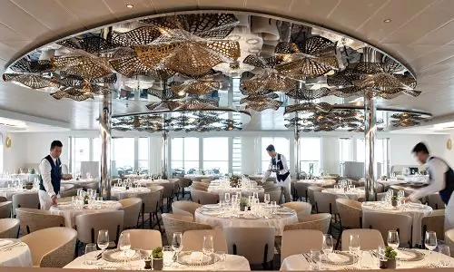 Gedeckte Tische und Servicekräfte im Panorama Restaurant auf dem Luxusschiff Le Bellot der Reederei Ponant