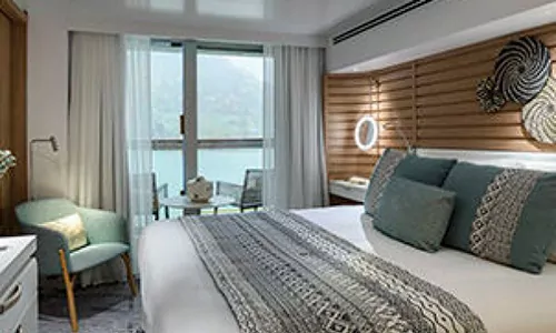 Prestige Suite Bett und Sitzbereichmit Blick auf Balkon auf dem Luxus Expeditionskreuzfahrtschiff Le Laperouse der Reederei Ponant