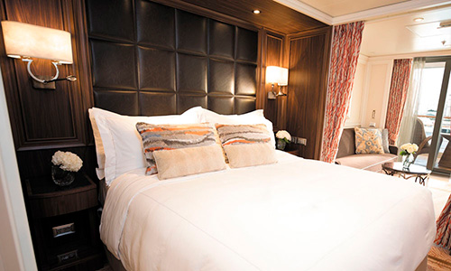 Seven Seas Explorer Bett im Queen-Size Format und Blick in Sitzbereich und Veranda in der Deluxe Veranda Suite