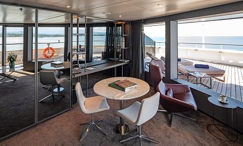 Tisch, Sessel und Blick auf Veranda mit Liegen in der Panoramasuite auf der Scenic Eclipse